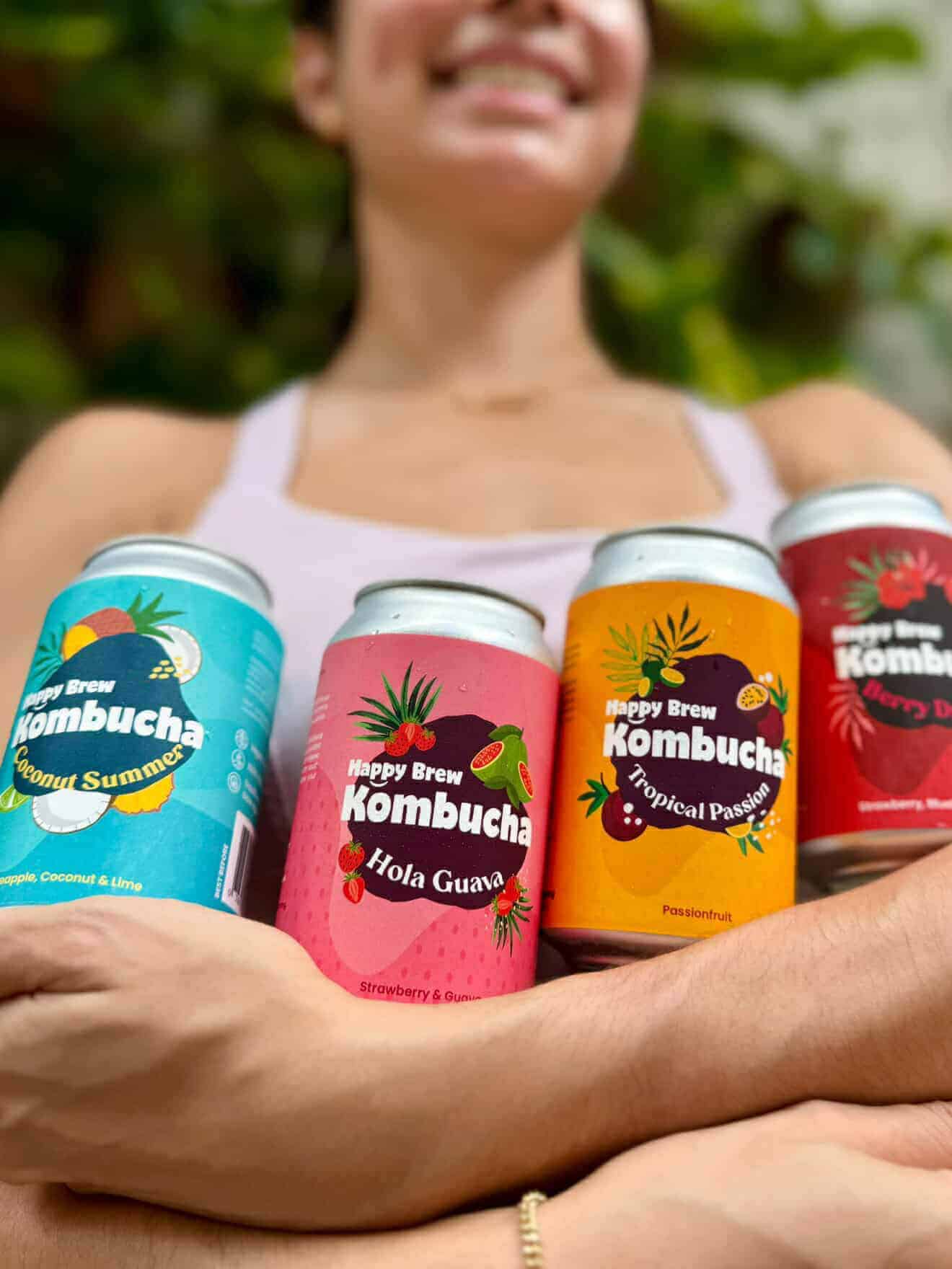Woman holding Happy Brew Kombucha cans in Manila, Philippines – locally crafted probiotic drinks in flavors Coconut Summer, Hola Guava, Tropical Passion, and Berry Dream